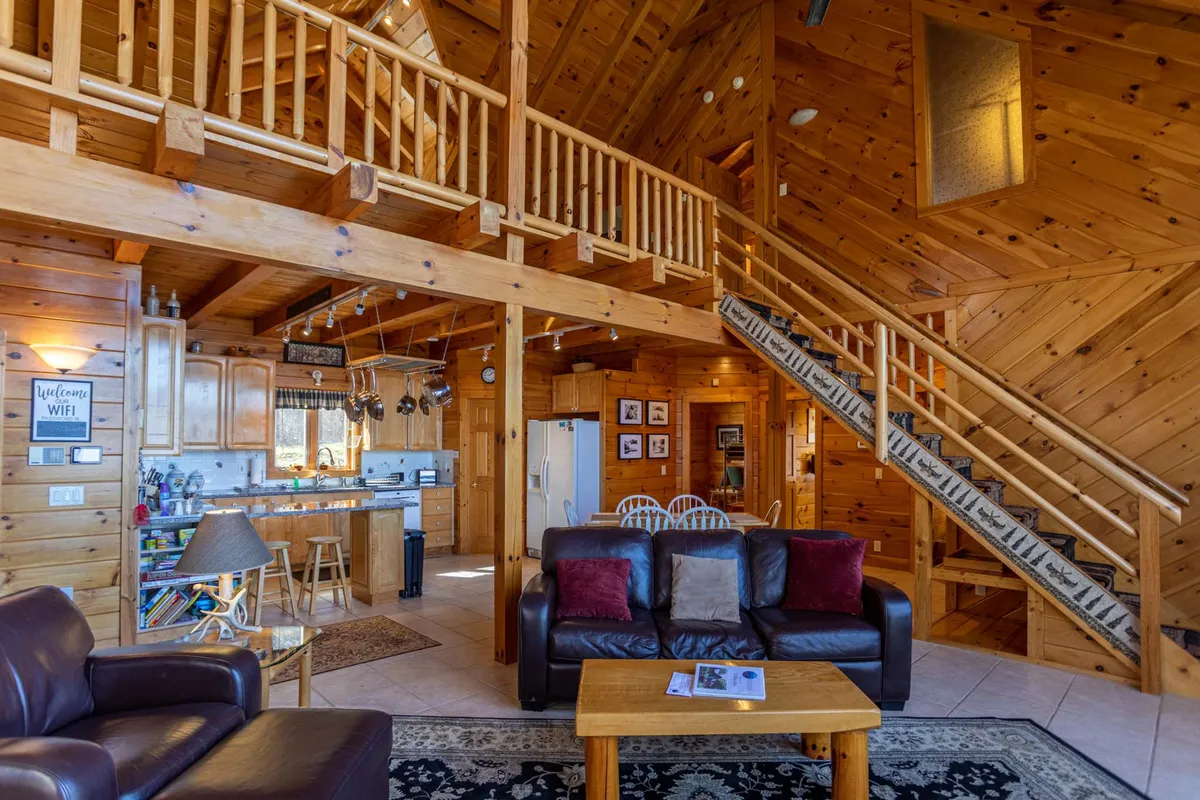 An interior view featuring exposed wooden beams, a cozy leather sofa, an open kitchen area, and a large dining table, designed for family gatherings and group activities. This space supports both cooking and game nights, with plenty of room for everyone.