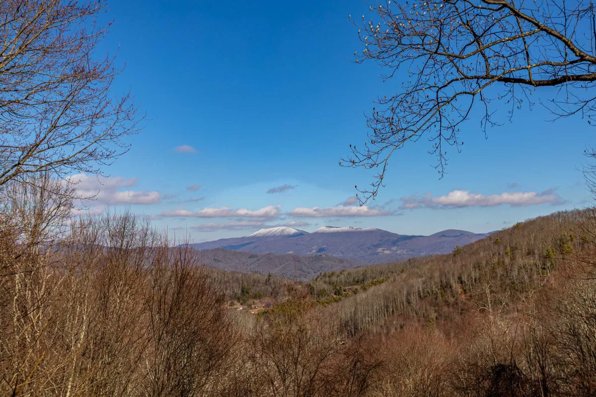 A breathtaking view of distant mountain ridges beneath a clear blue sky, with scattered clouds enhancing the sense of depth and vastness. The vantage point suggests a high elevation, ideal for hiking and nature observation, immersing the viewer in the tranquil beauty of the Blue Ridge Mountains.