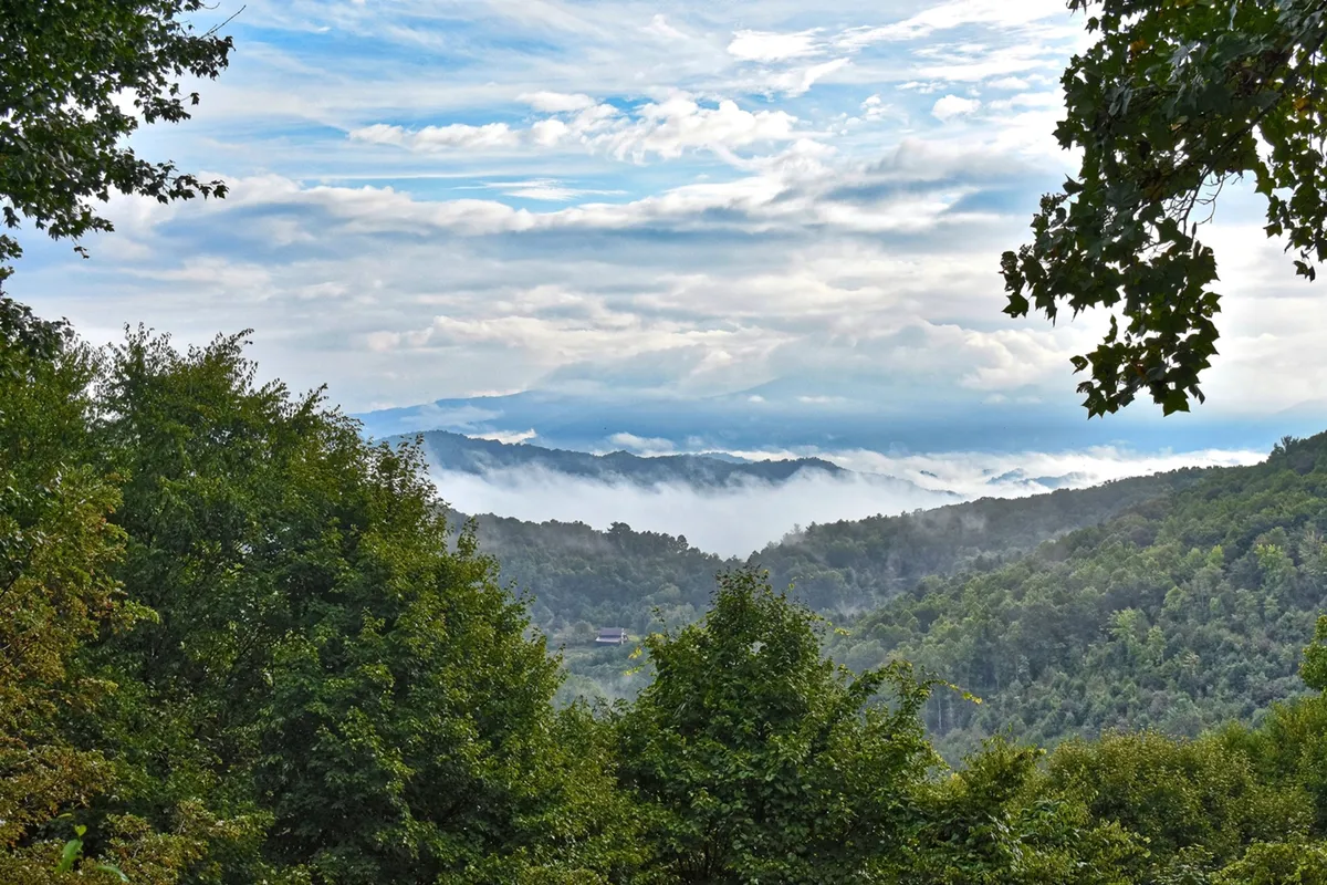 A sweeping view of a lush, green mountain range under dramatic cloud cover, suggesting the pristine natural environment and sense of adventure waiting just outside the door. The image evokes the promise of hiking, exploring, and wildlife sightings in the area.