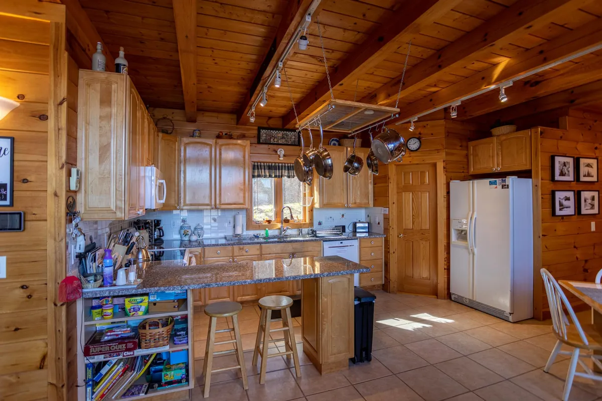Another view of a functional kitchen with granite countertops, wooden cabinetry, hanging pots, a kitchen island, and a window awash with natural light. The space feels intimate and practical, ideal for both everyday meals and special occasions.
