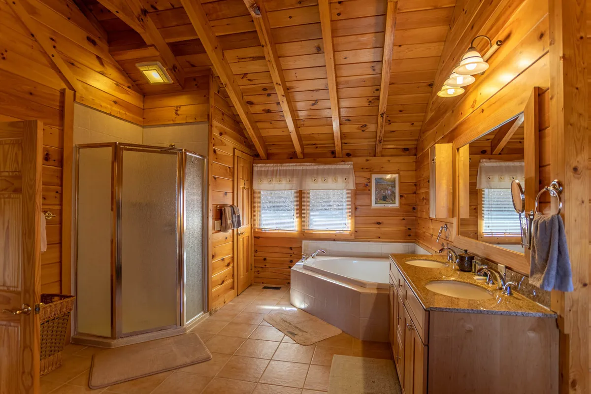 A modern bathroom with a spacious walk-in shower, elegant double sink vanity, and a standalone bathtub. Natural light filters through, highlighting the clean lines, wooden ceiling, and tranquil design—providing a serene spot to refresh and recharge.