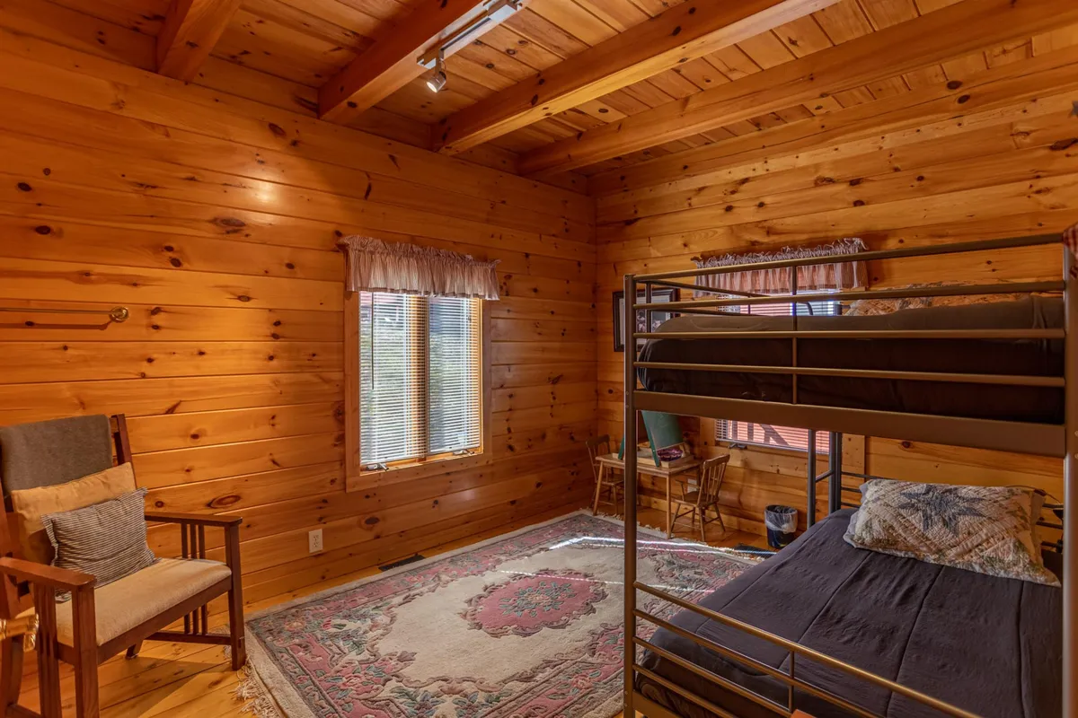 A welcoming guest bedroom with classic wooden walls, a set of bunk beds, a cozy rug, and a comfortable chair. Soft morning light streams in, creating an atmosphere of warmth and versatility for families or friends sharing the space.